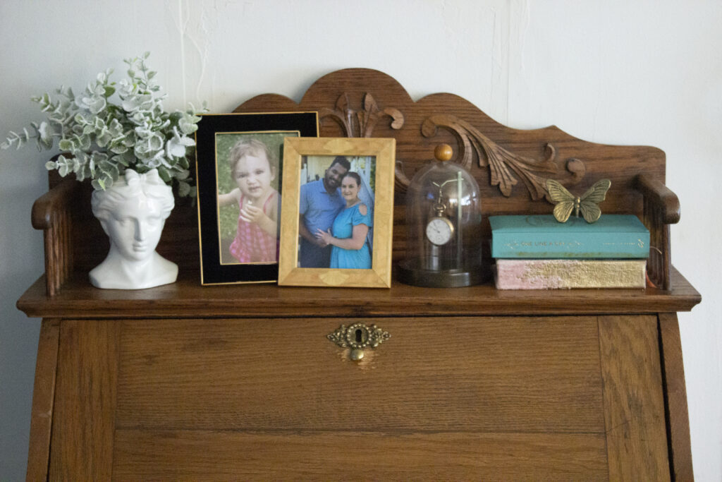 Vintage secretary desk styled with a bust, two photo frames, a vintage pocket watch, books, and a butterfly