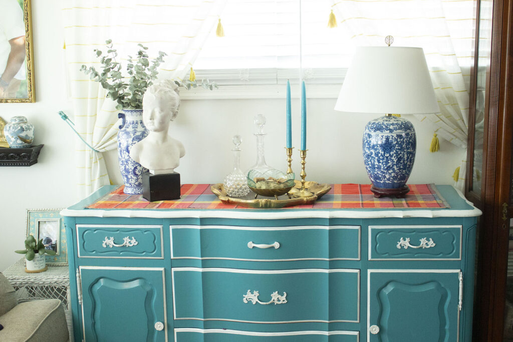 Turquoise blue buffet table styled with a blue and white porcelain lamp, bust statue, and decanters