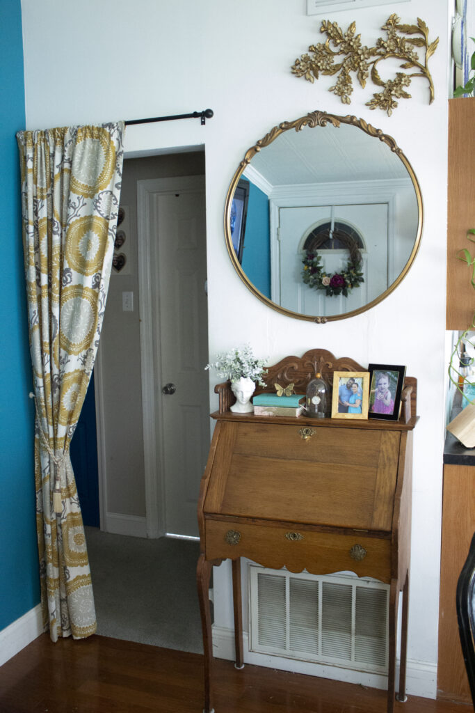 Vintage secretary desk styled in maximalist fashion with a mirror and a curtain over a doorway