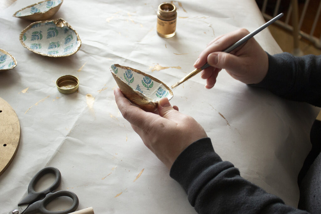Person painting gold rims on seashells