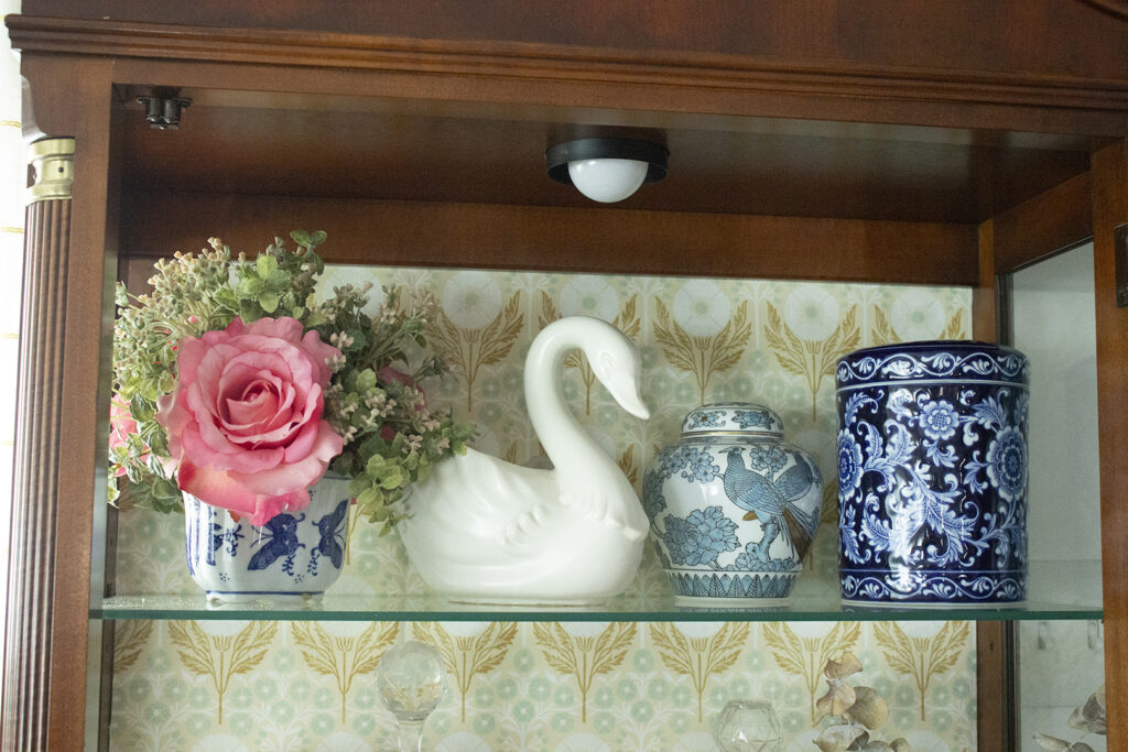 shelf of china cabinet with floral arrangement, ginger jar, swan vase, and blue jar
